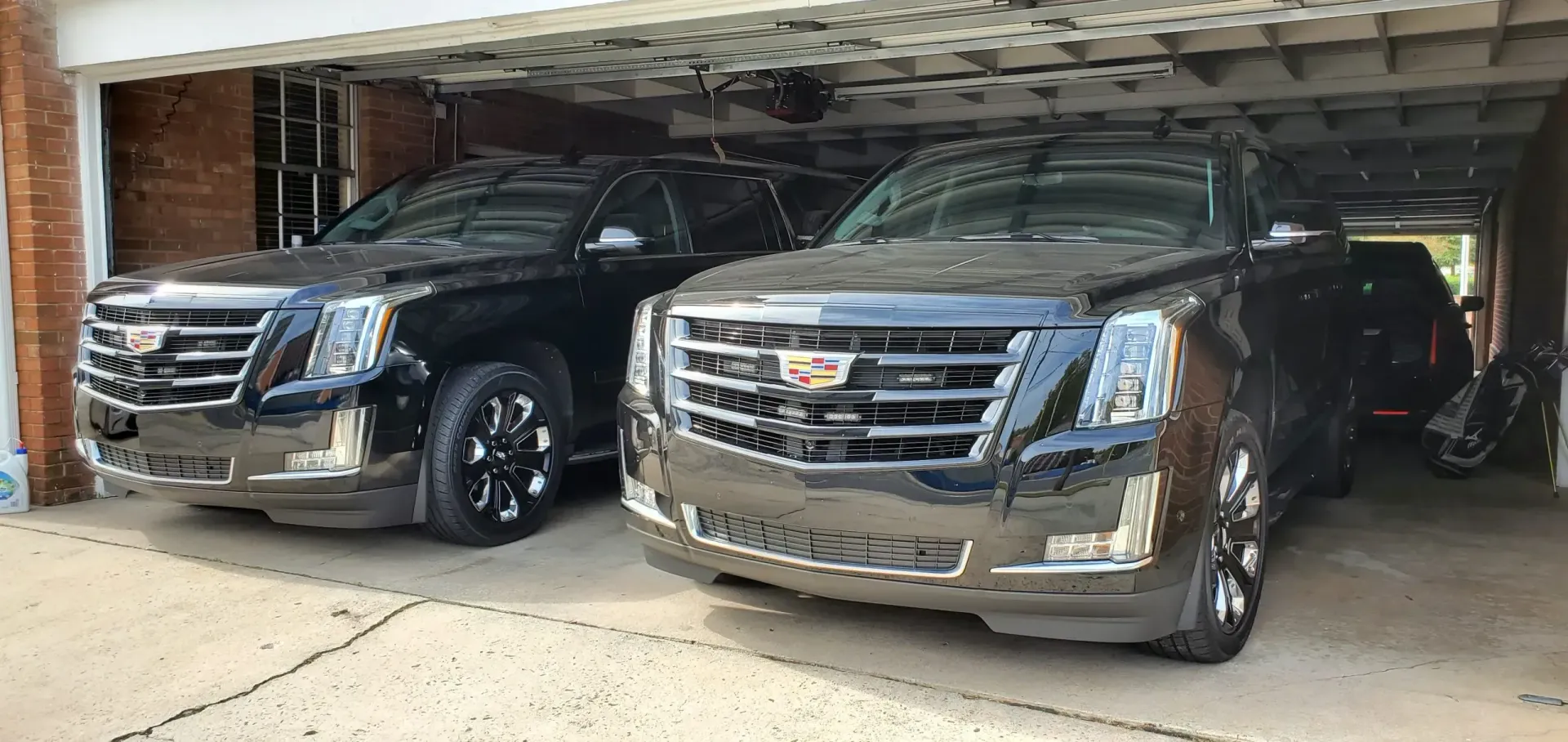 Two black Cadillac Escalades parked inside a garage.