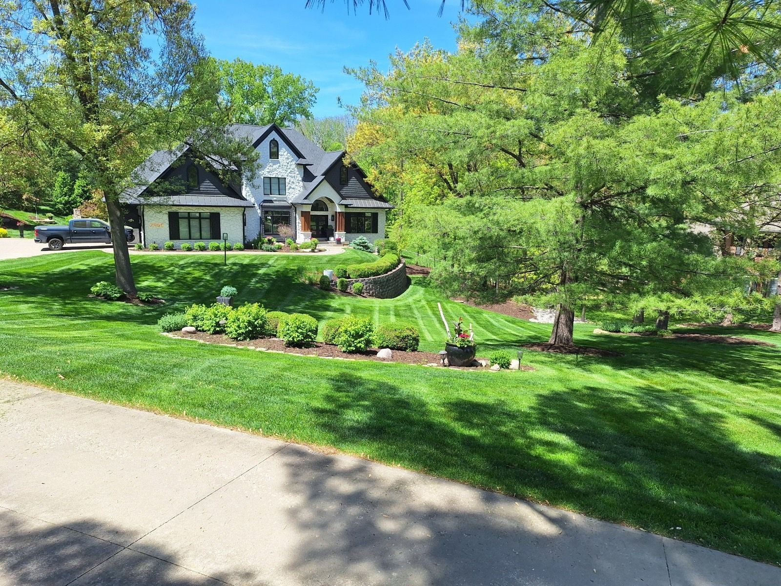 A two-story house with black trim sits on a green, well-manicured lawn with trees.