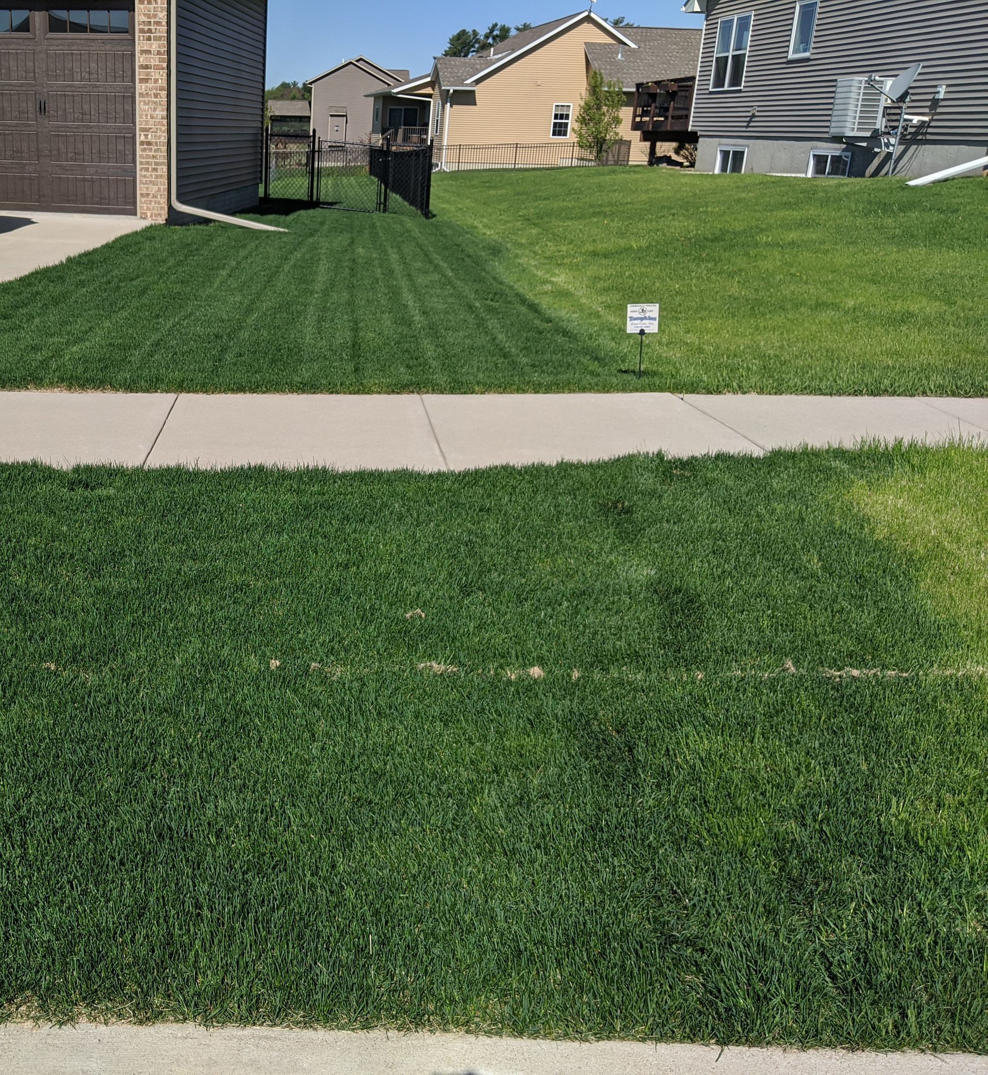 Green lawn next to a sidewalk and a house with a garage door. Mowed lawn has stripes.