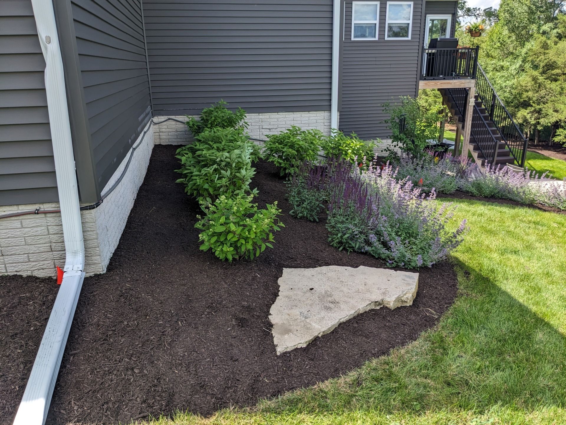 There is a large rock in the middle of the garden in front of the house.