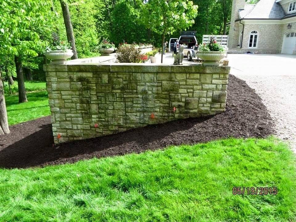 A stone wall is in the middle of a lush green lawn in front of a house.