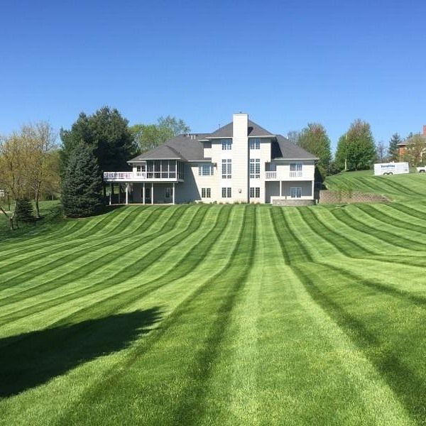 A large house is sitting on top of a hill with a lush green lawn in front of it.