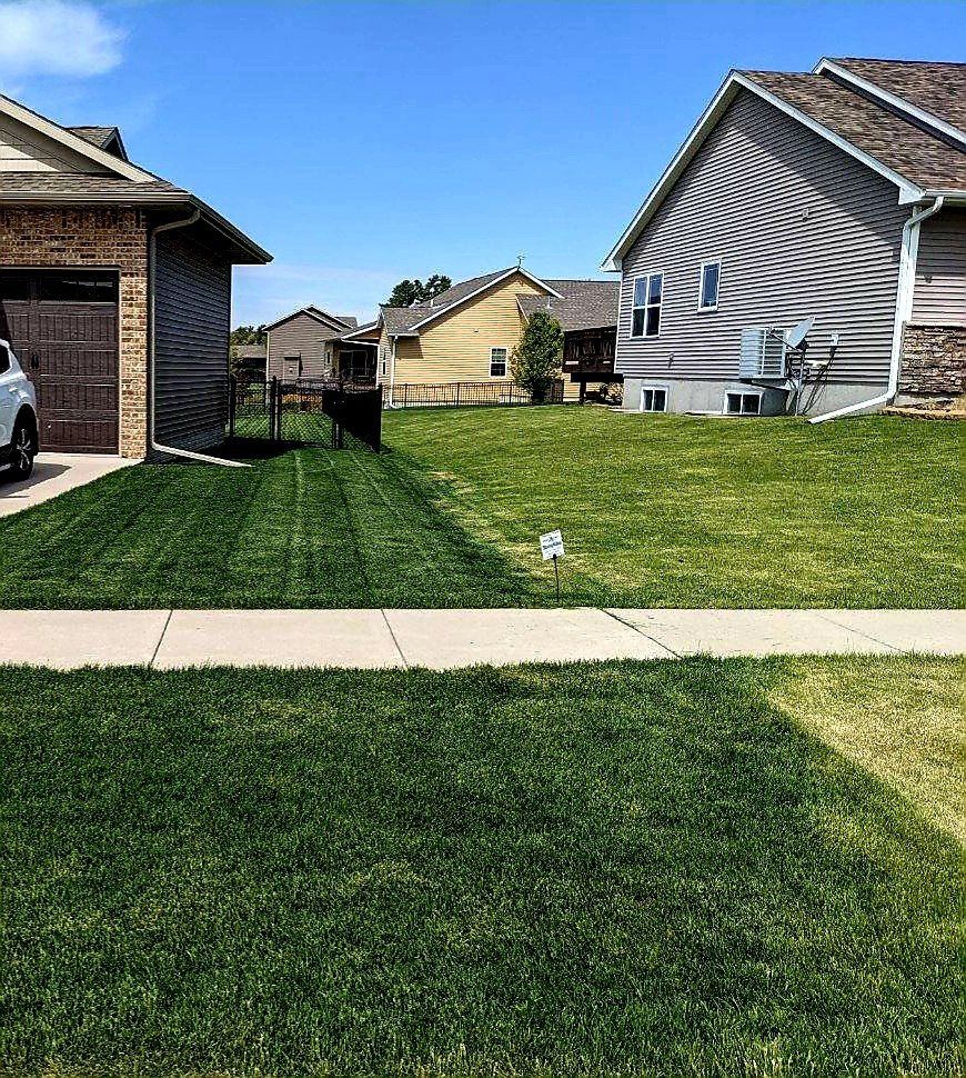 A car is parked in front of a house next to a lush green lawn.