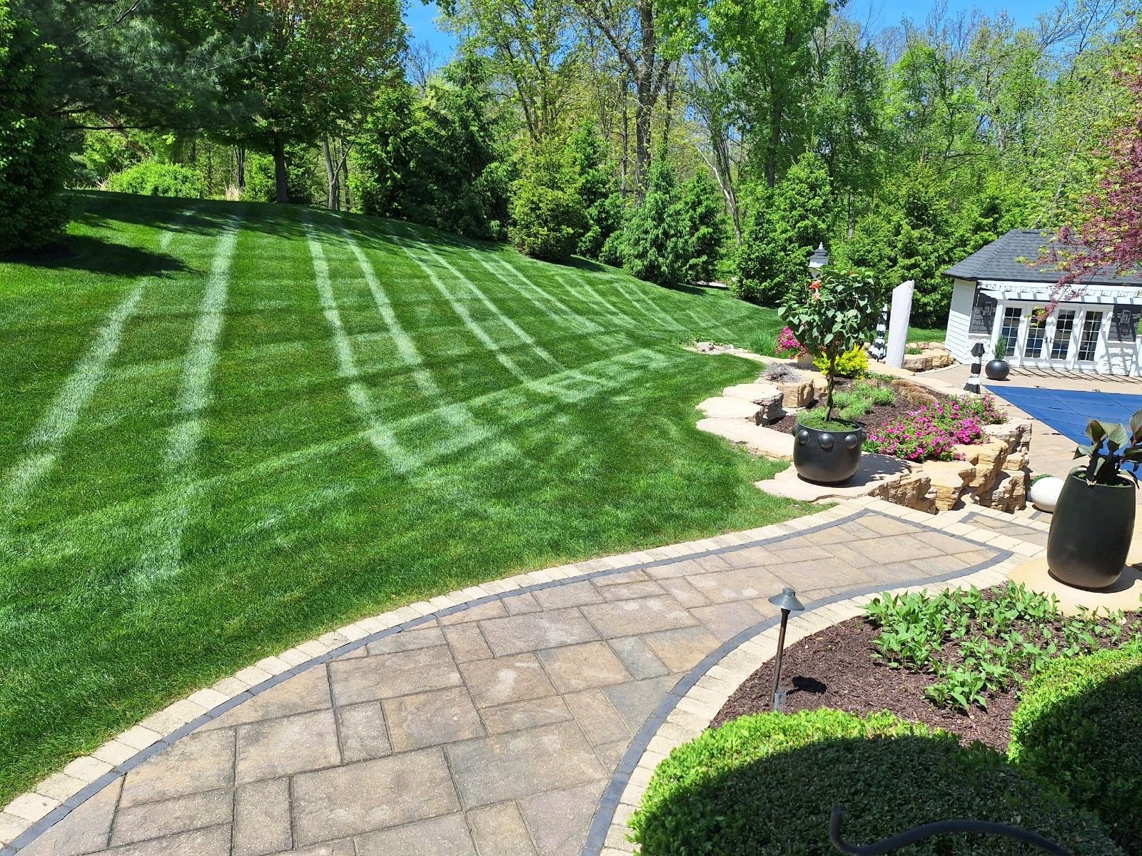 A brick walkway leading to a lush green lawn with a gazebo in the background.