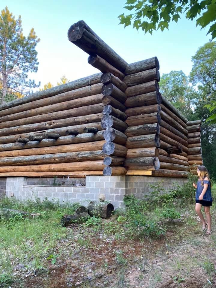 A woman is standing in front of a log cabin.