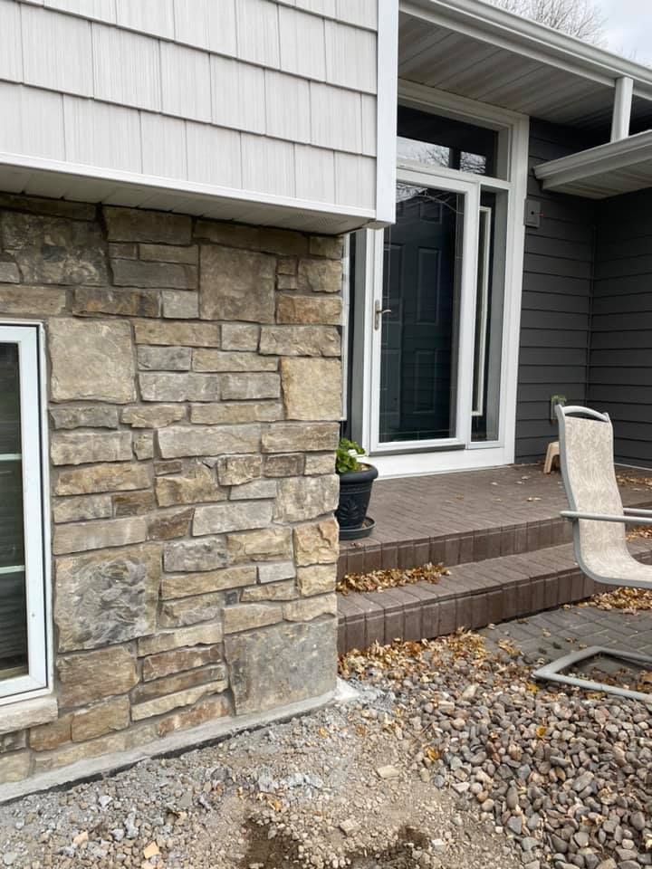 The front of a house with a stone wall and a black door.