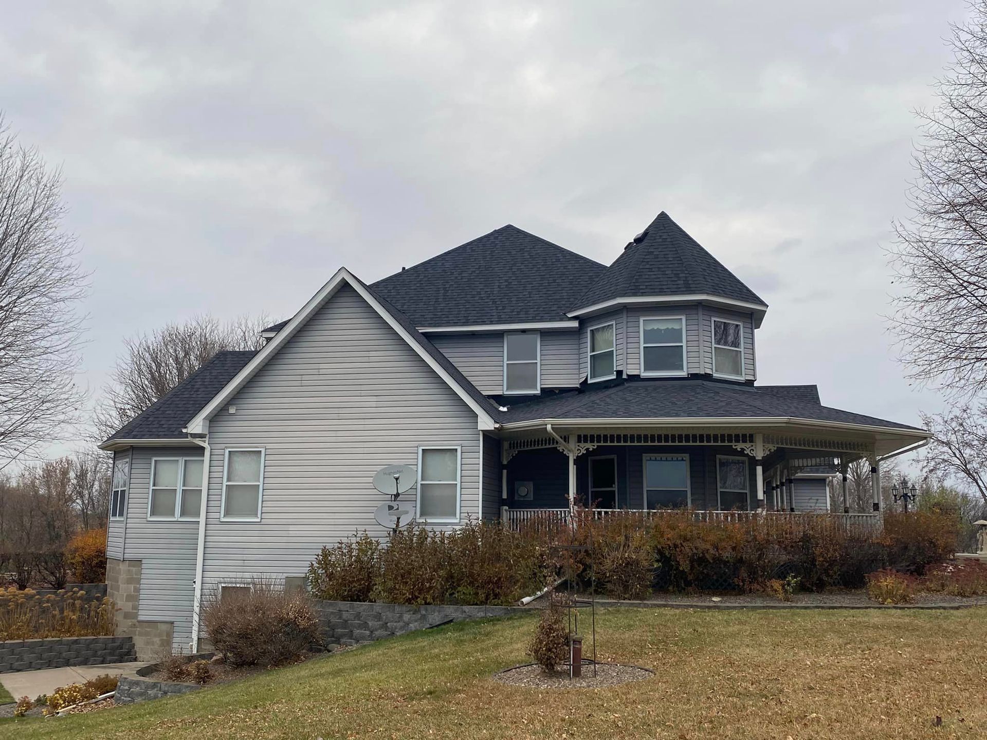 A large white house with a black roof is sitting on top of a grassy hill.