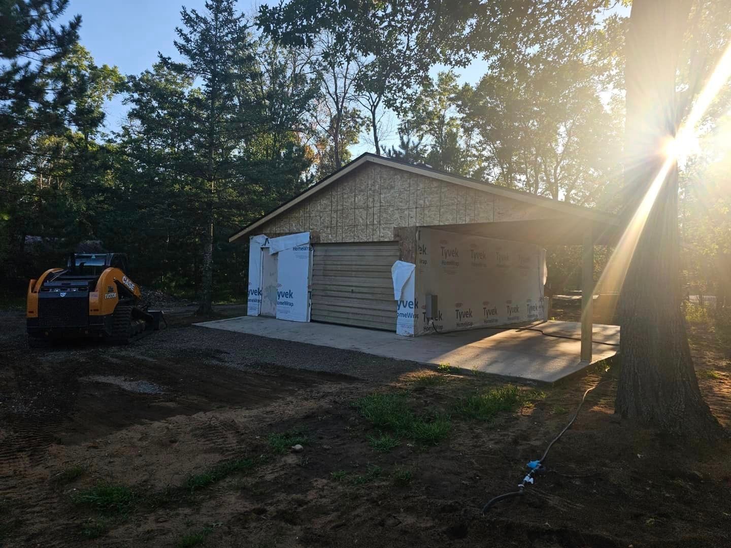 The sun is shining through the trees behind a garage under construction.