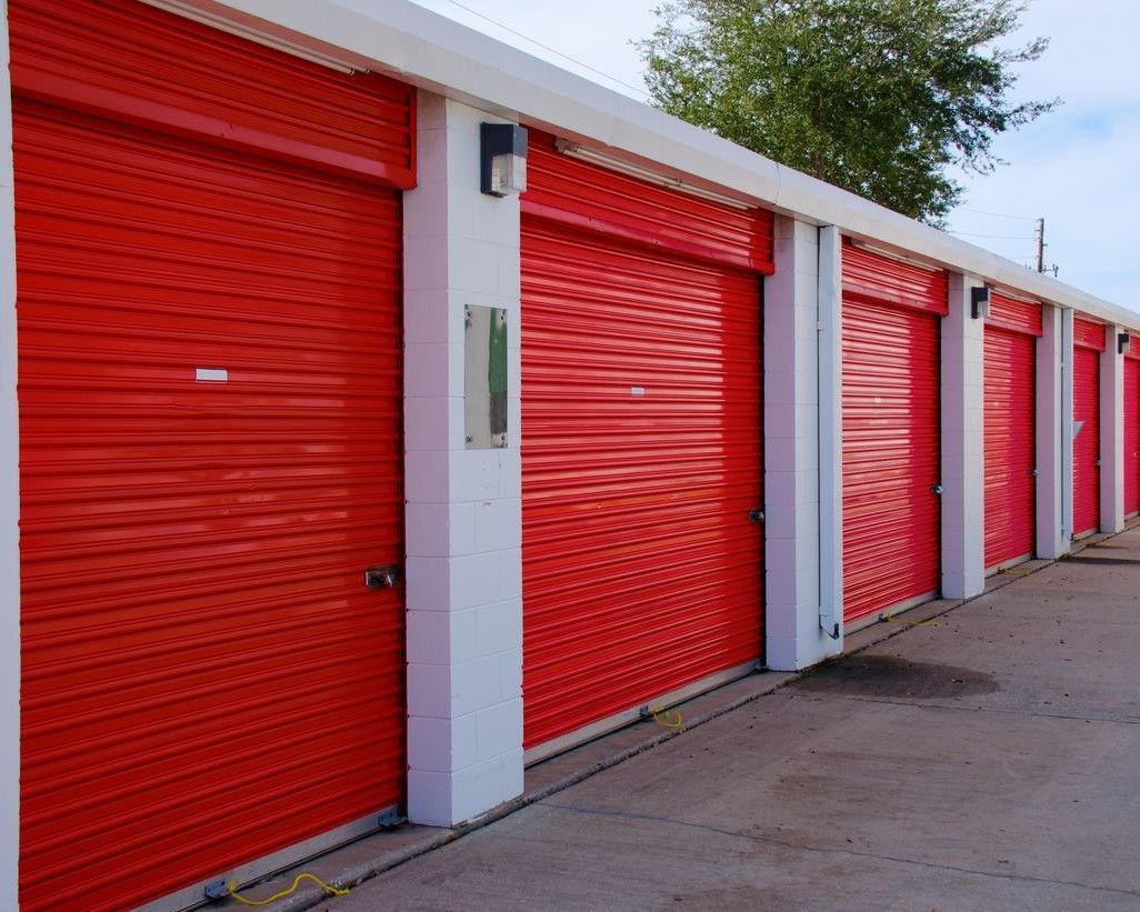 Red storage unit doors in a row, white trim, outdoor setting.