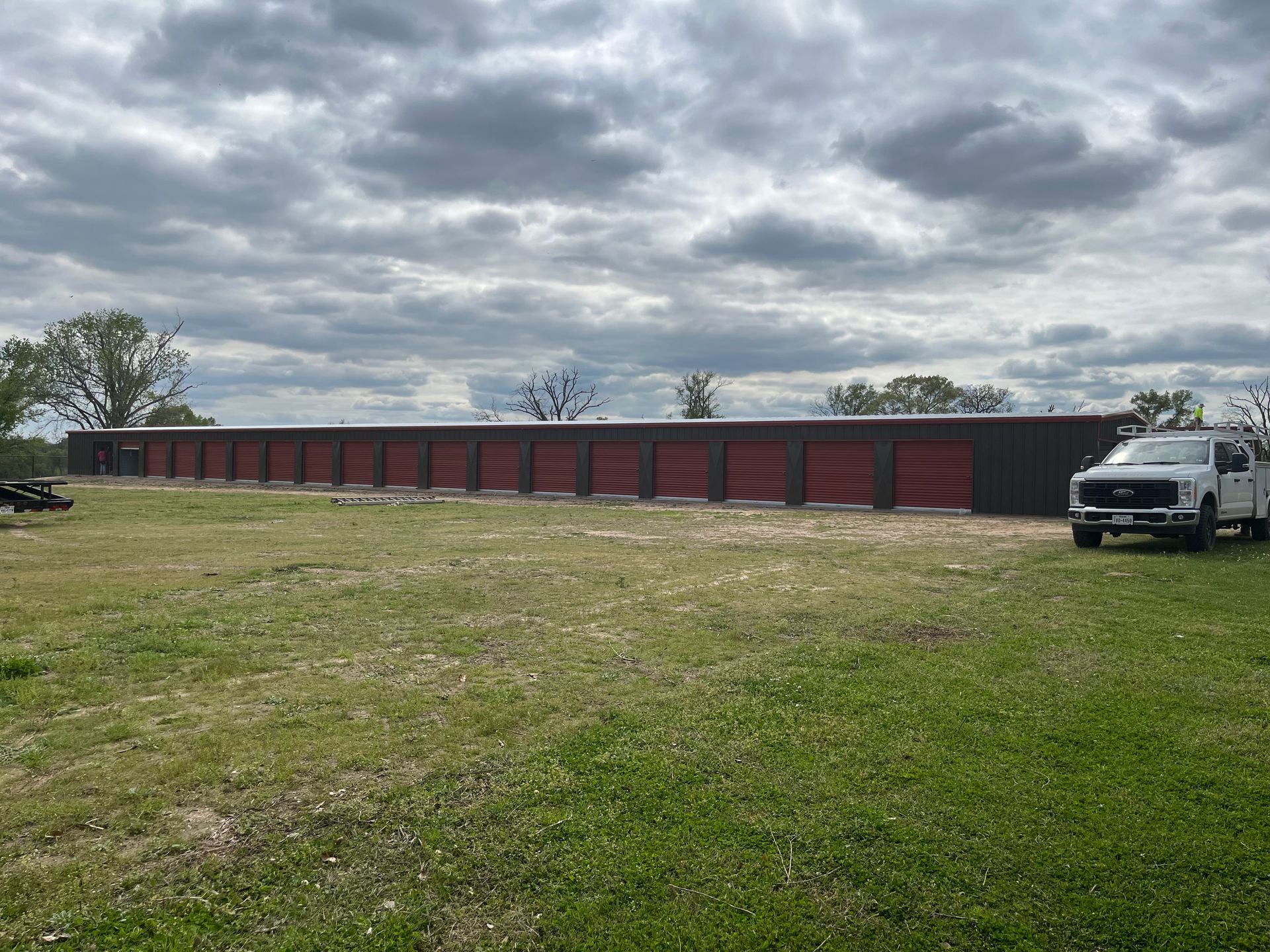 Long, dark red building with a wavy design on a grassy field, a white truck is parked nearby under a cloudy sky.