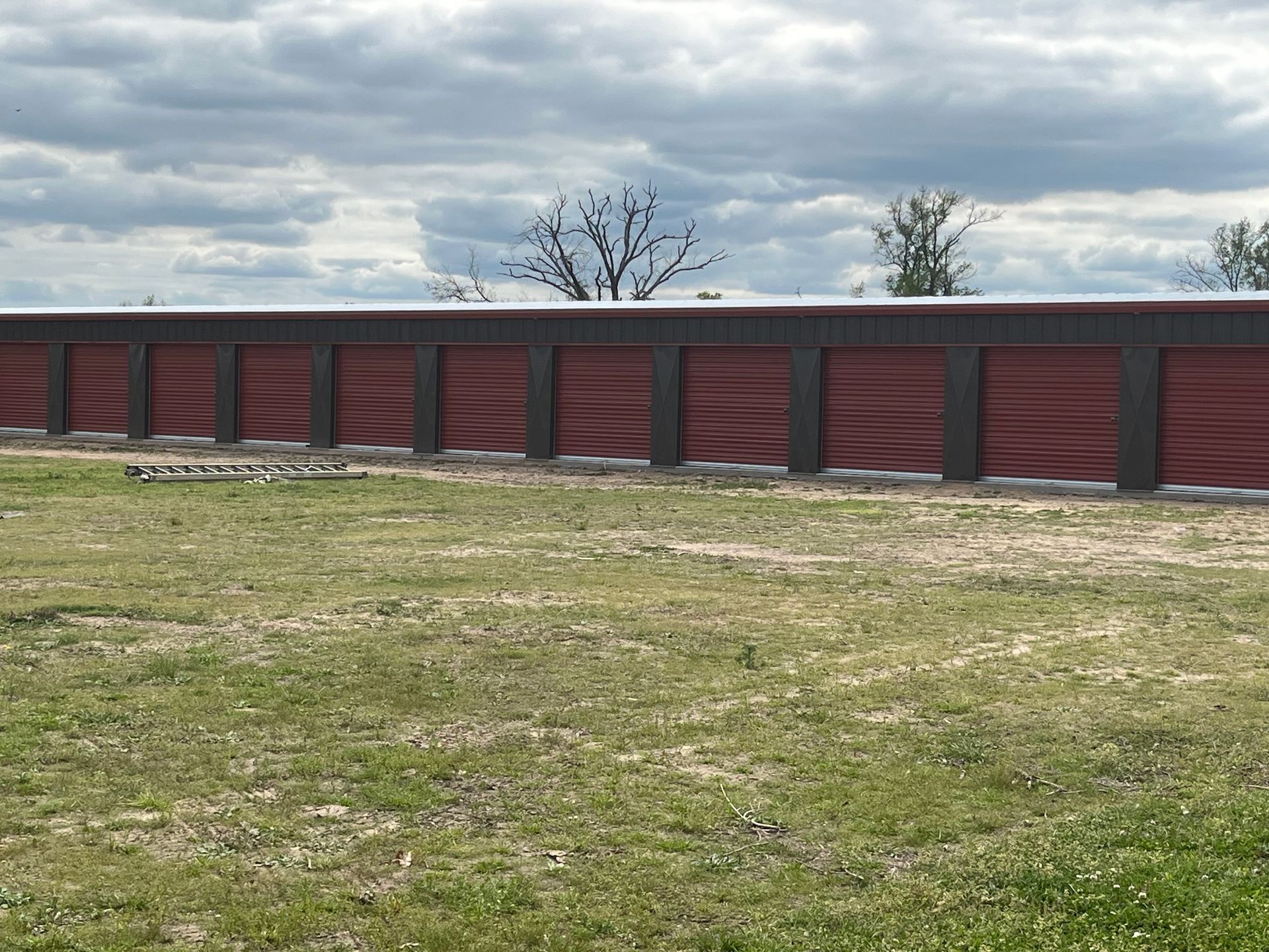 Row of red storage units under a cloudy sky. Green grass in the foreground.