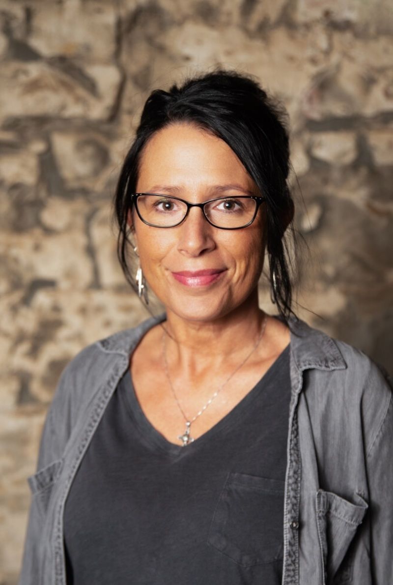 A woman wearing glasses and a gray shirt is smiling for the camera.