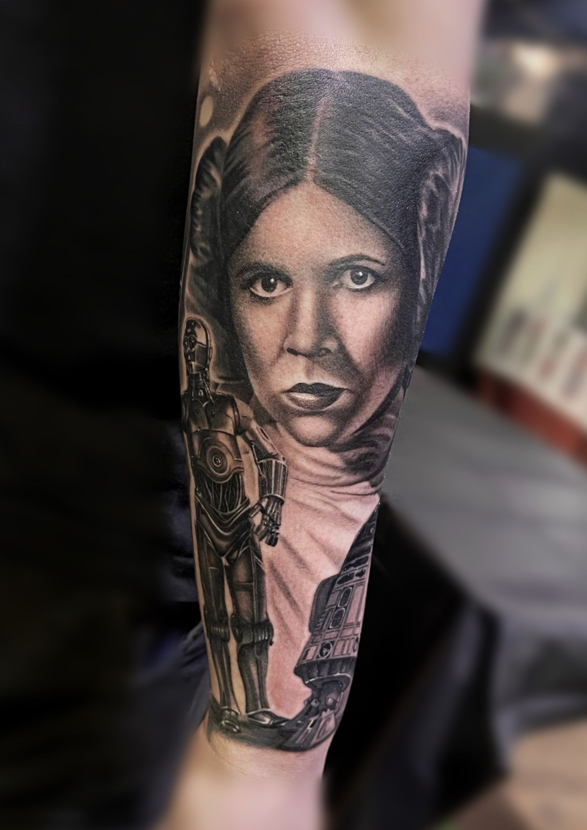 A black and white tattoo of a woman and a robot on a forearm.