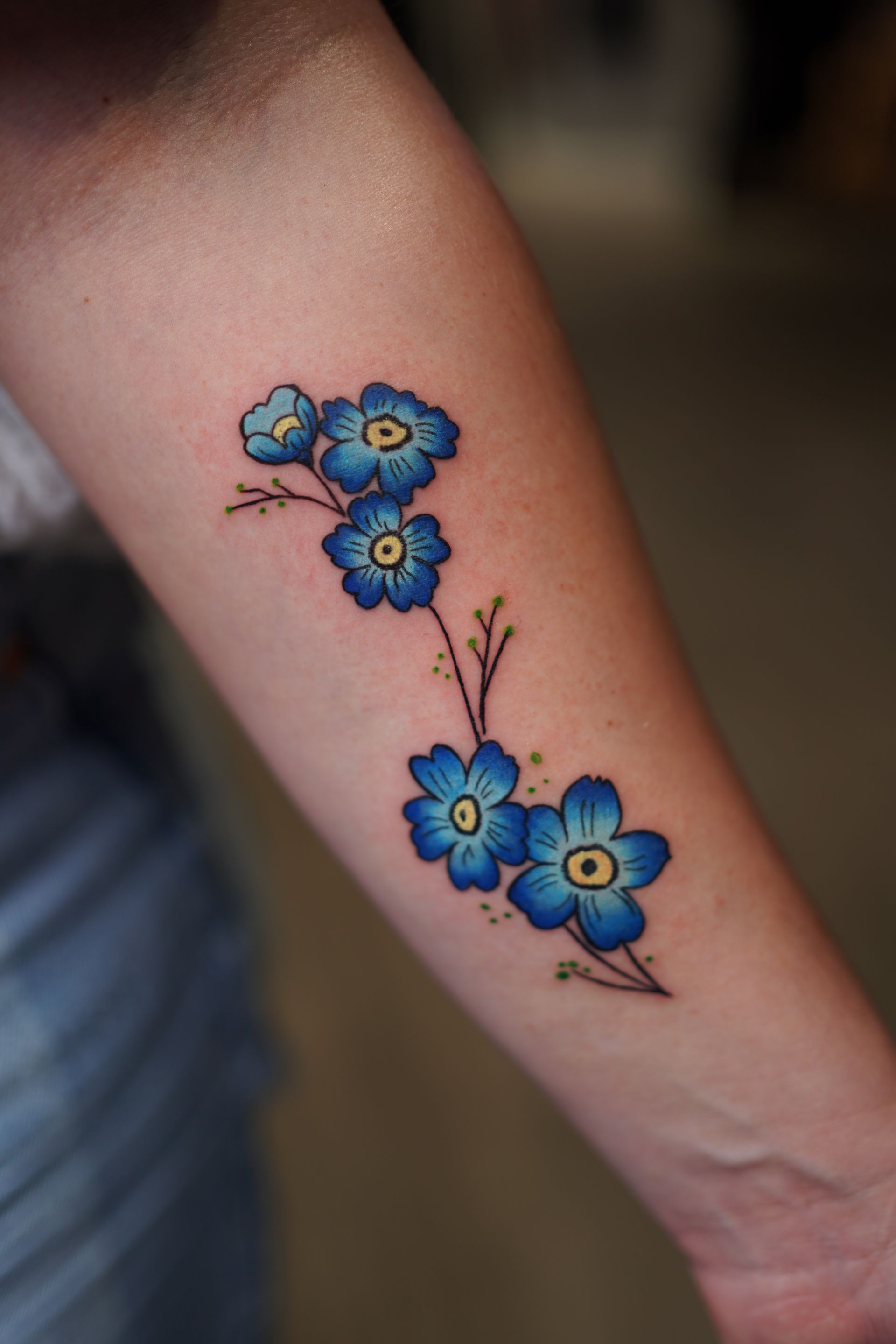 A woman has a tattoo of blue flowers on her forearm