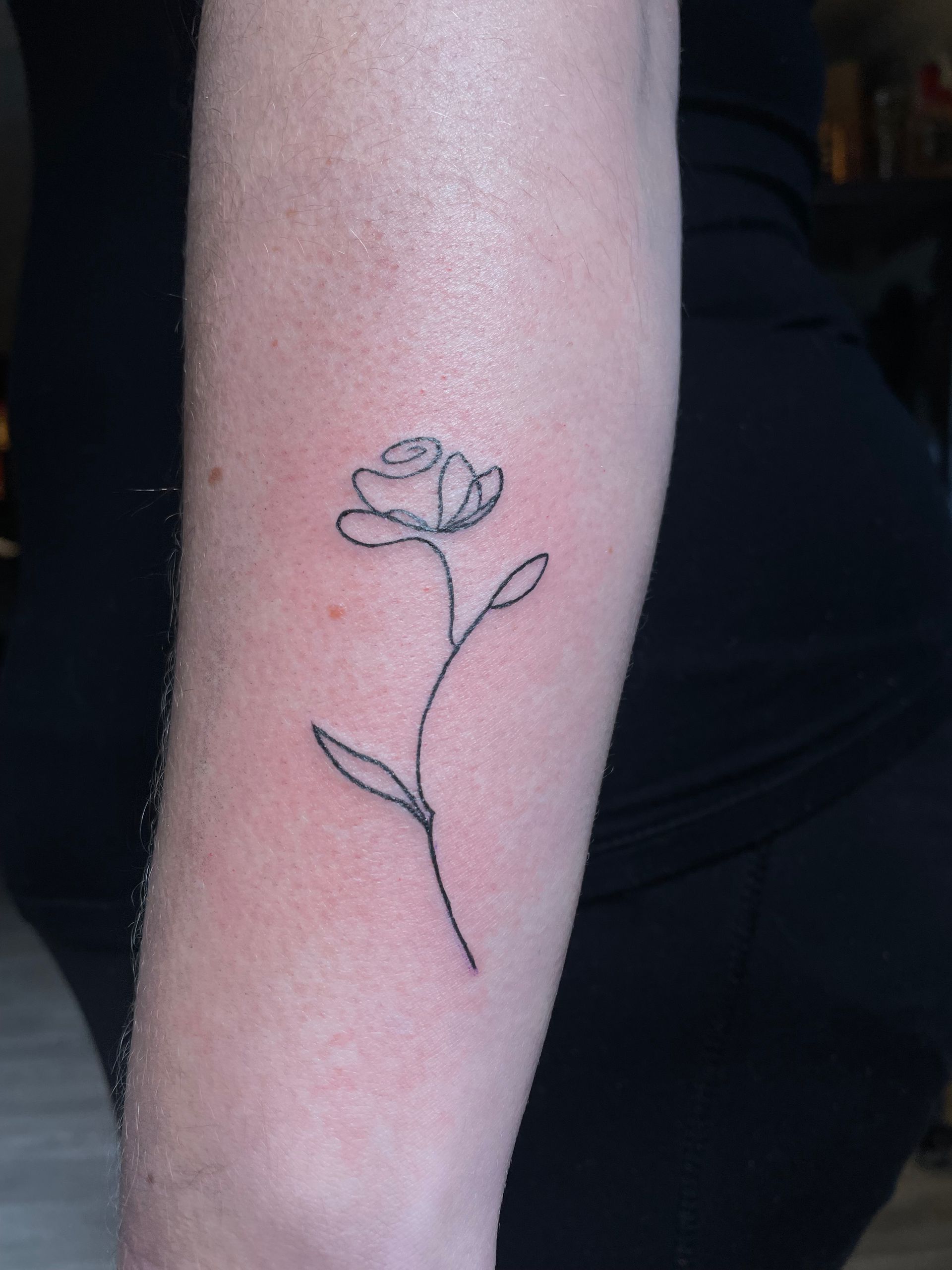 A person has a small tattoo of a rose on their forearm.