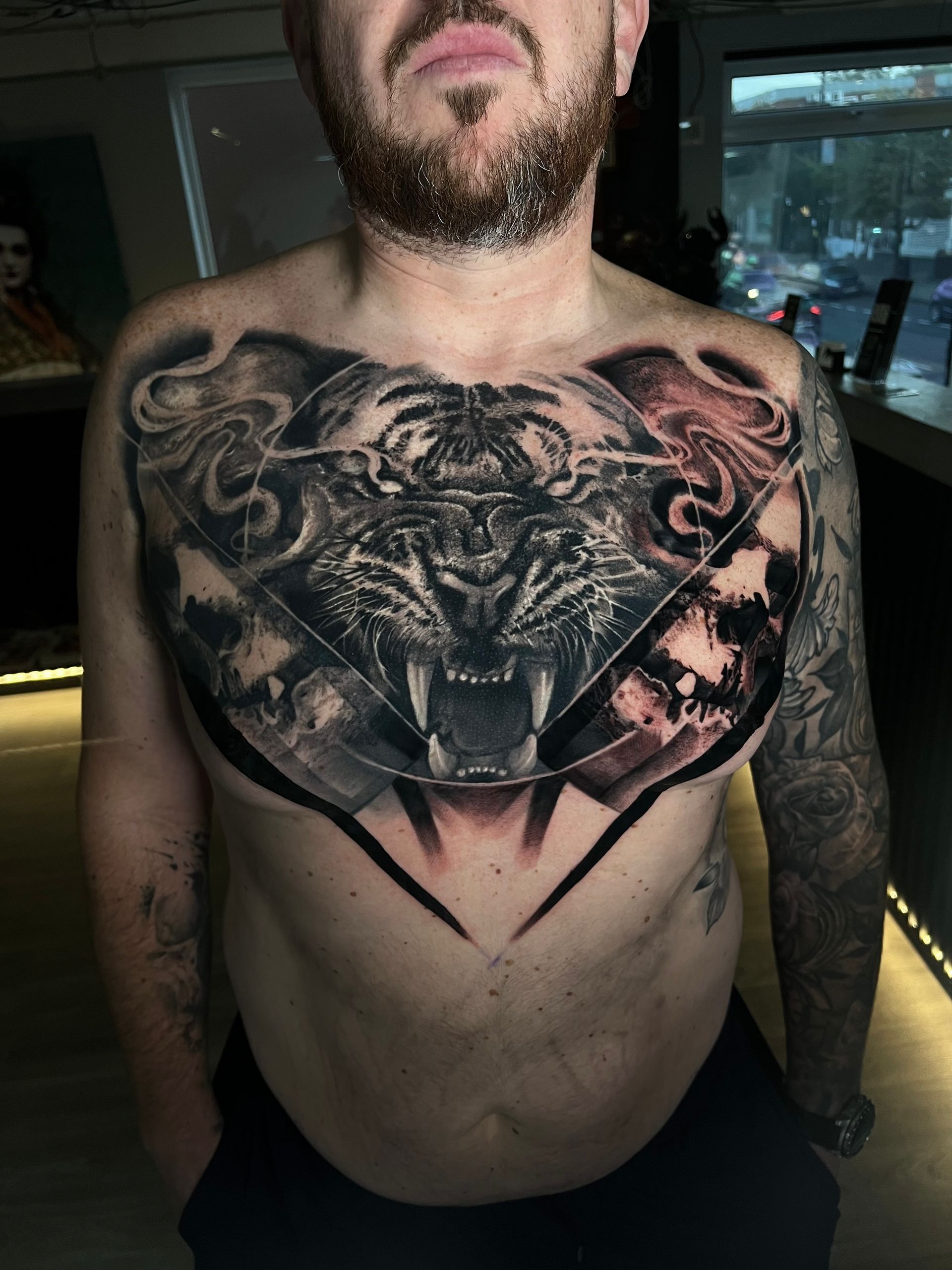 A man with a beard has a tattoo of a tiger on his chest.