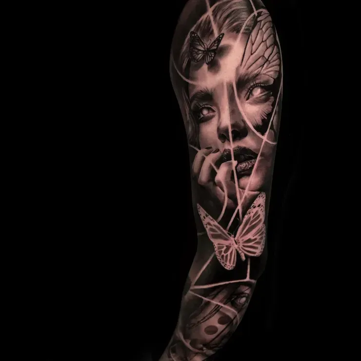 A black and white tattoo of a woman 's face with butterflies on her arm.