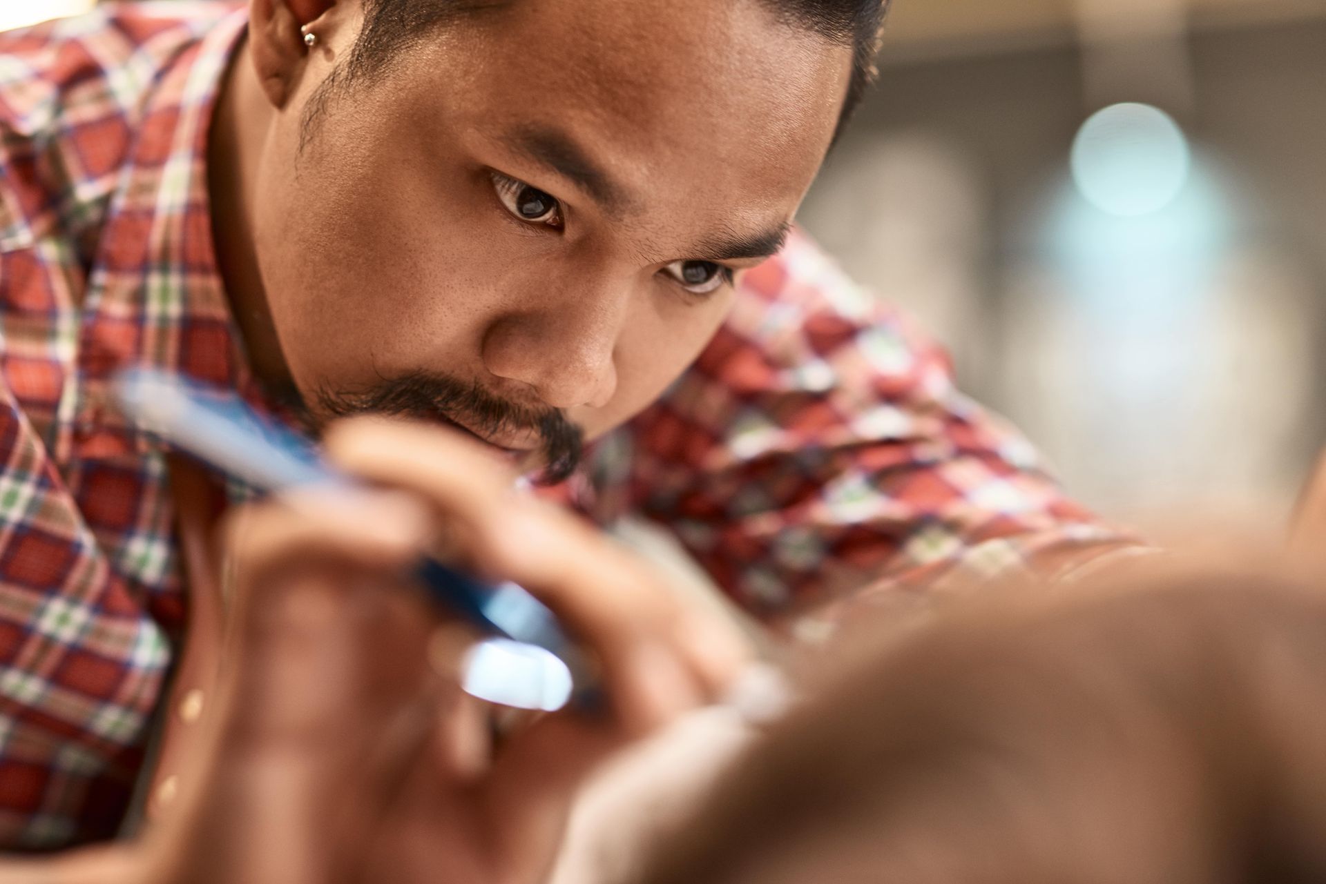 A man in a plaid shirt is holding a pen in his mouth.