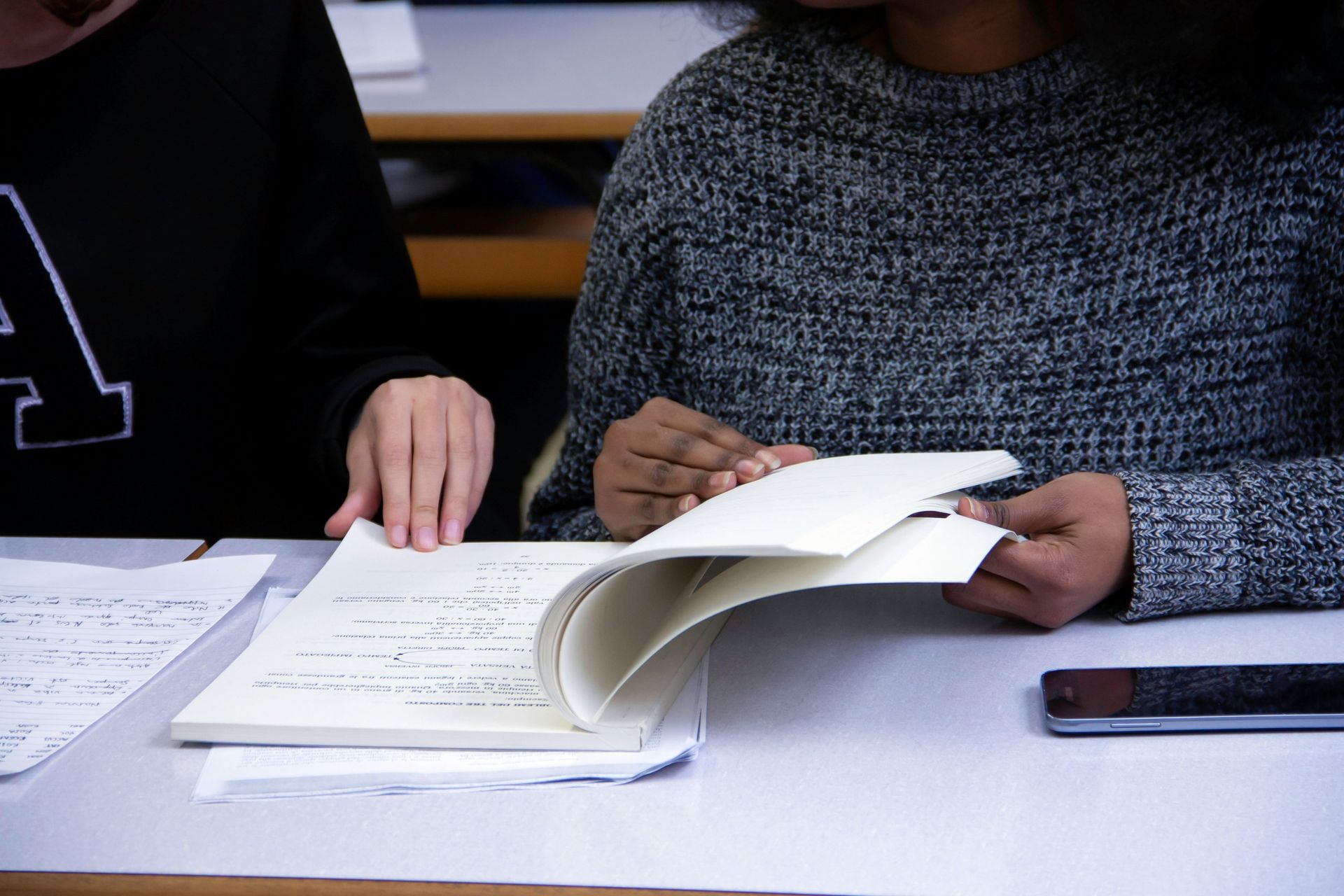 Two people are sitting at a table reading a book.