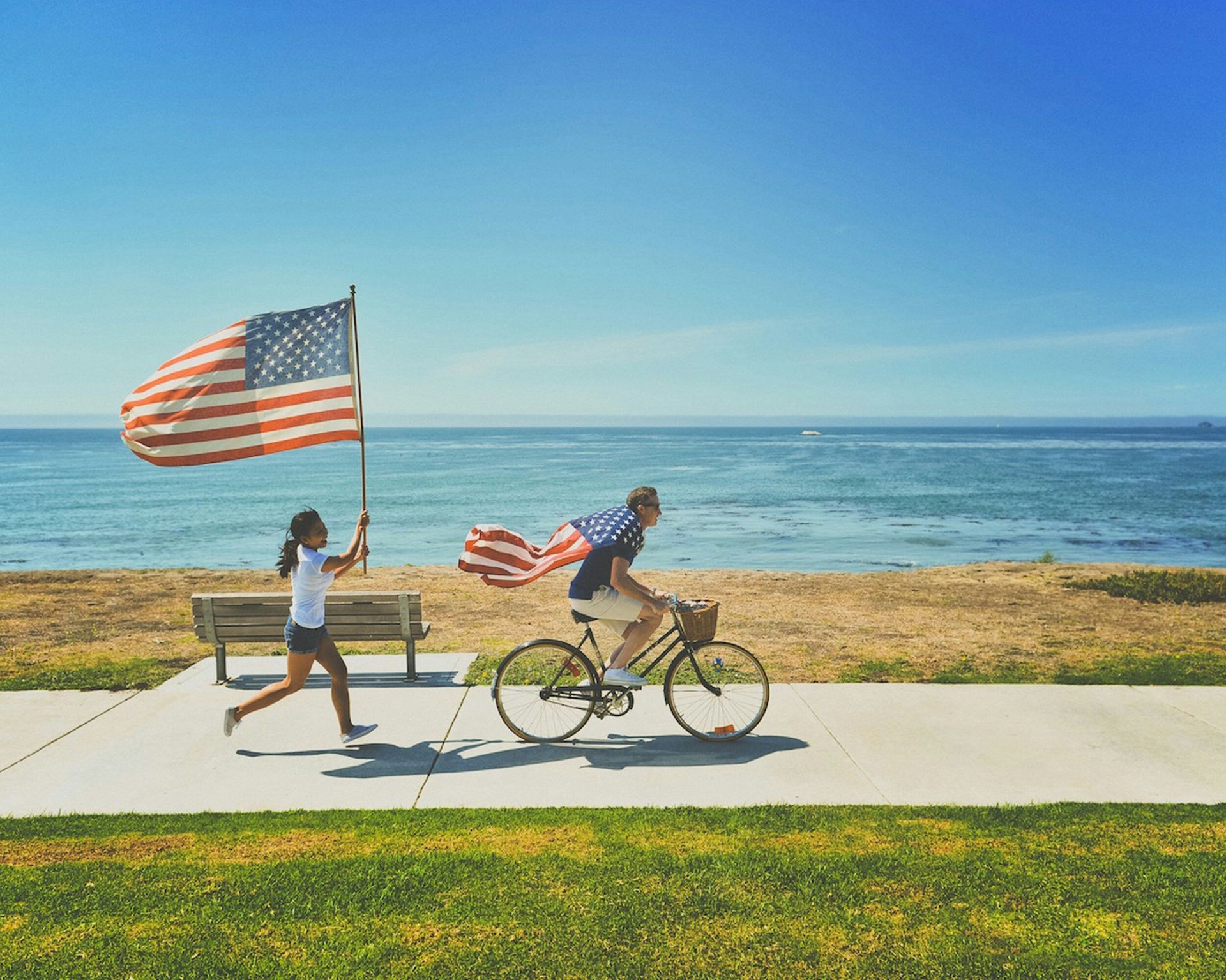 A man is riding a bike while a woman holds an american flag.