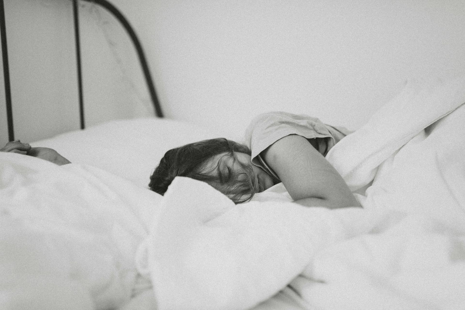 A woman is sleeping in a bed with white sheets and pillows.