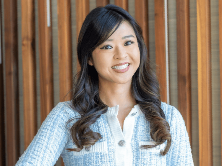 A woman is standing in front of a shelf with her arms crossed and smiling.