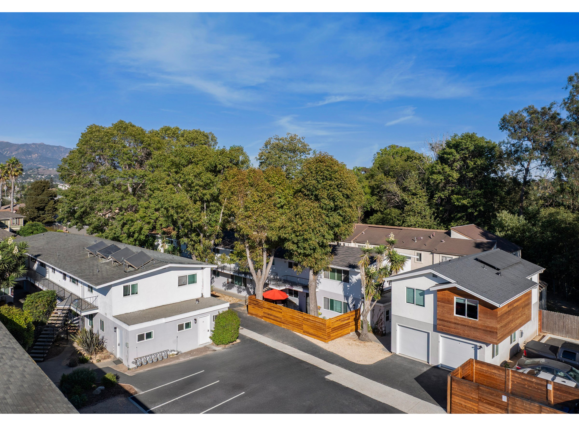 Apartment buildings with parking lot and surrounding trees under a blue sky.