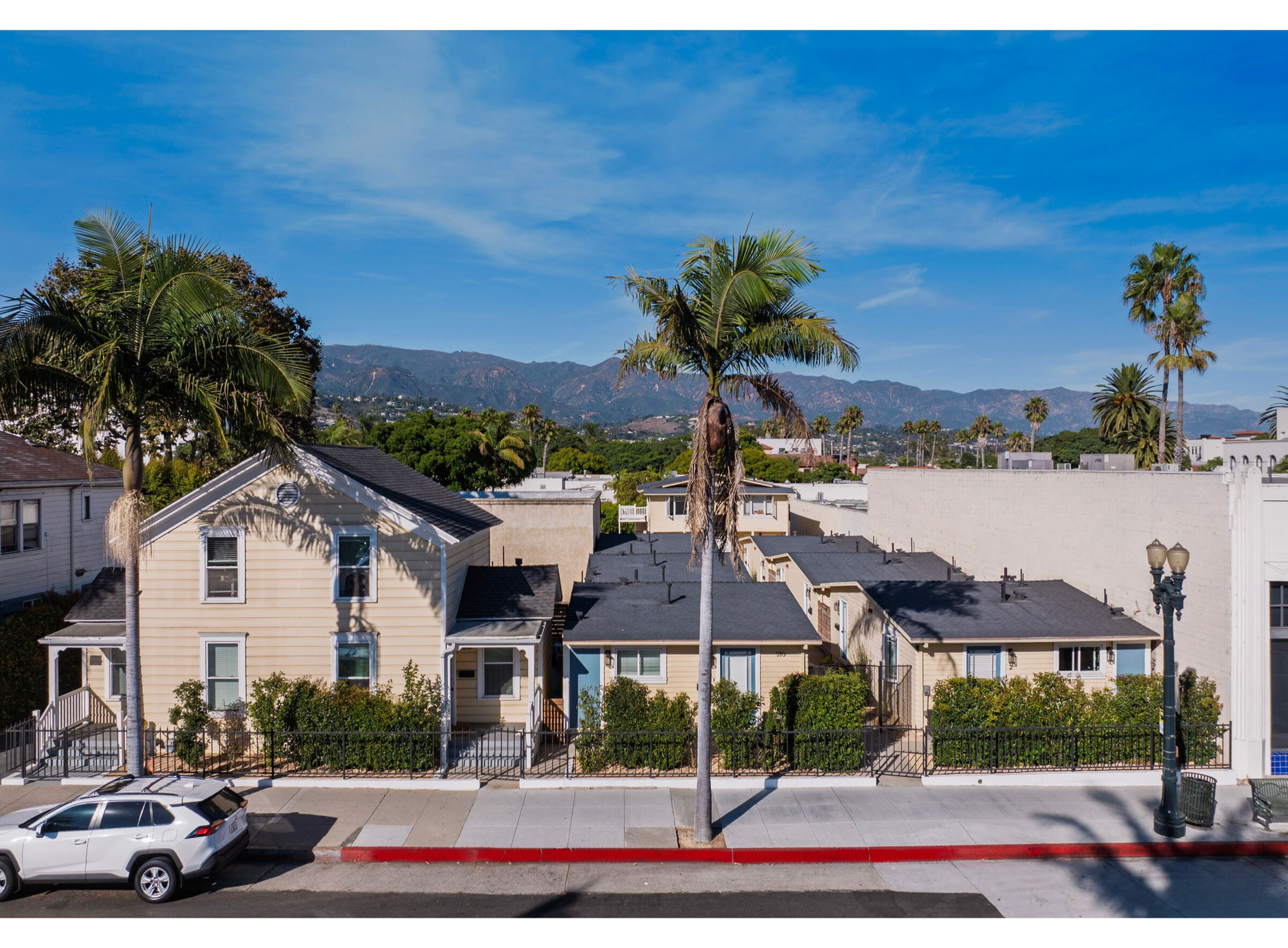Buildings with beige siding, palm trees, and mountain backdrop, street view, sunny day.