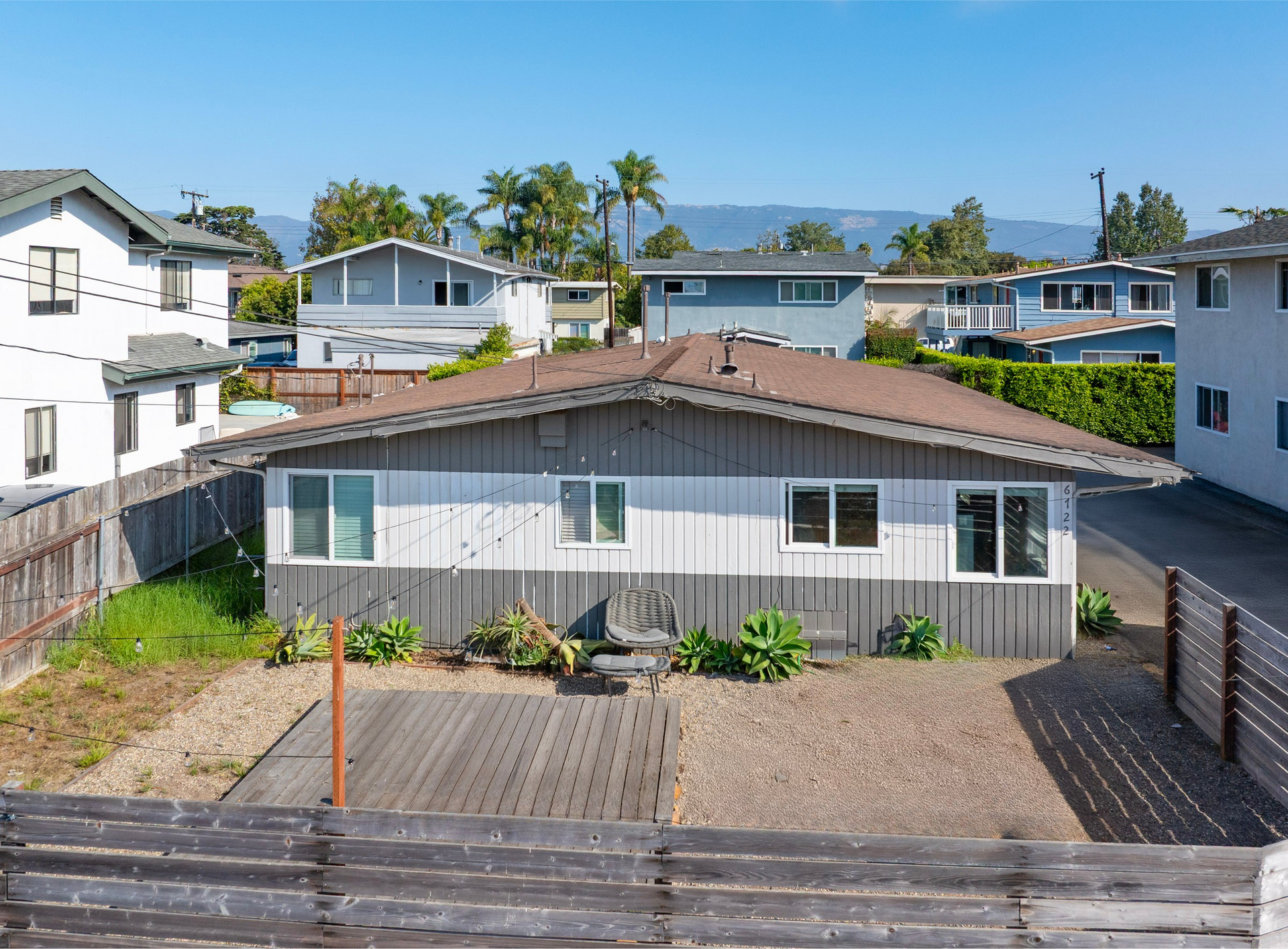 A single-story, gray and white house with a brown roof and a wooden deck.