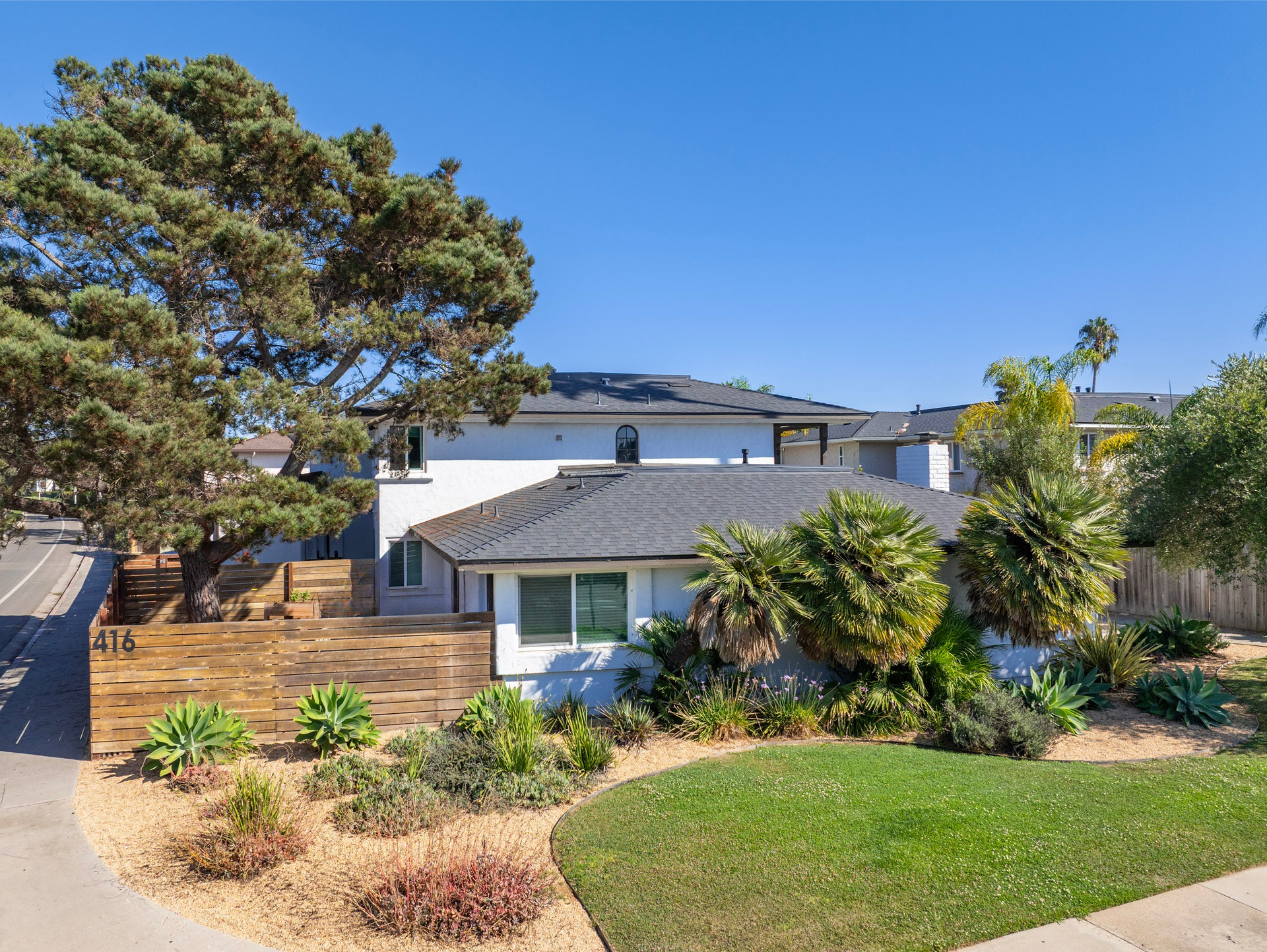 White house with dark roof and landscaping under a blue sky.