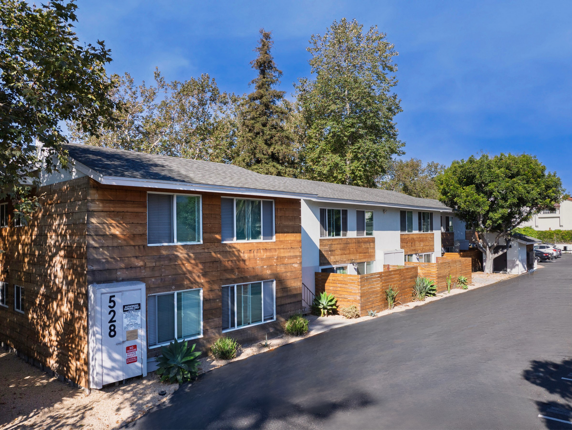 Two-story apartment building with wood siding, gray shutters, and a paved driveway.