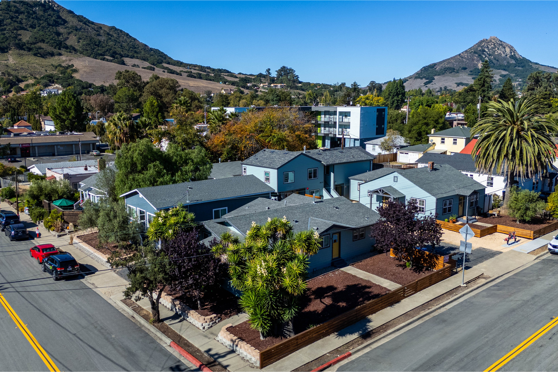 Aerial view of several blue houses on a corner lot, with mountains in the background and a sunny day.