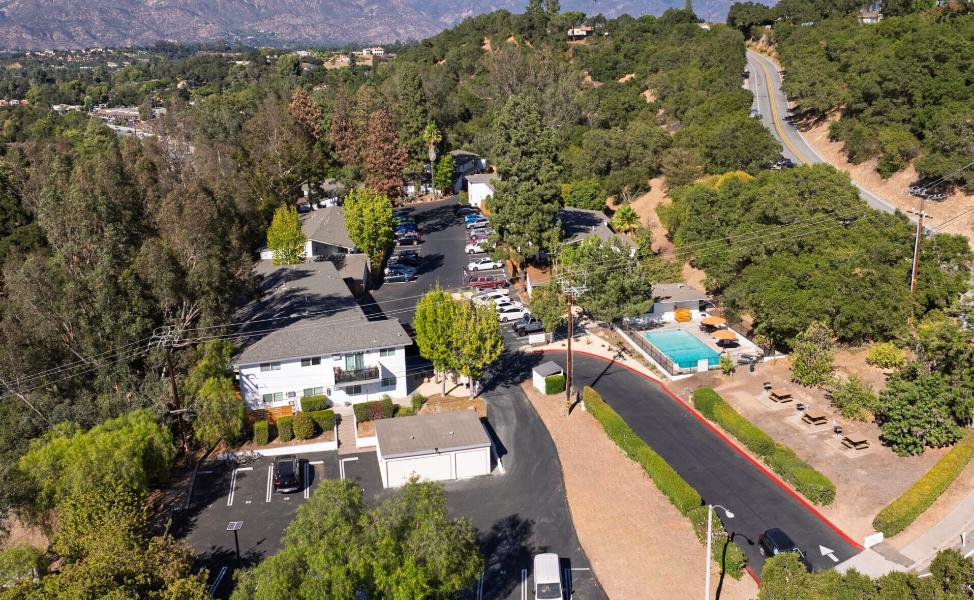 Two-story building with white upper level and wood-paneled lower level, palm trees, walkway, and gravel.