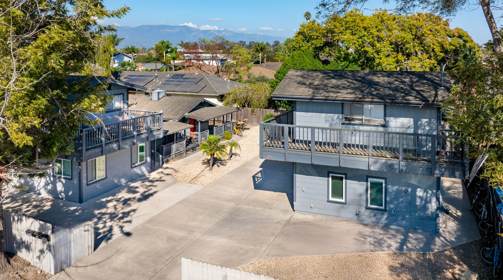 Two-story gray houses with balconies and a shared concrete driveway under a clear sky.