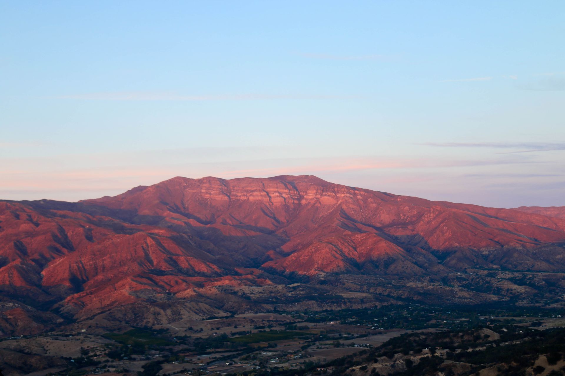 Mountain range at sunset, lit by golden light with a pale blue sky overhead.