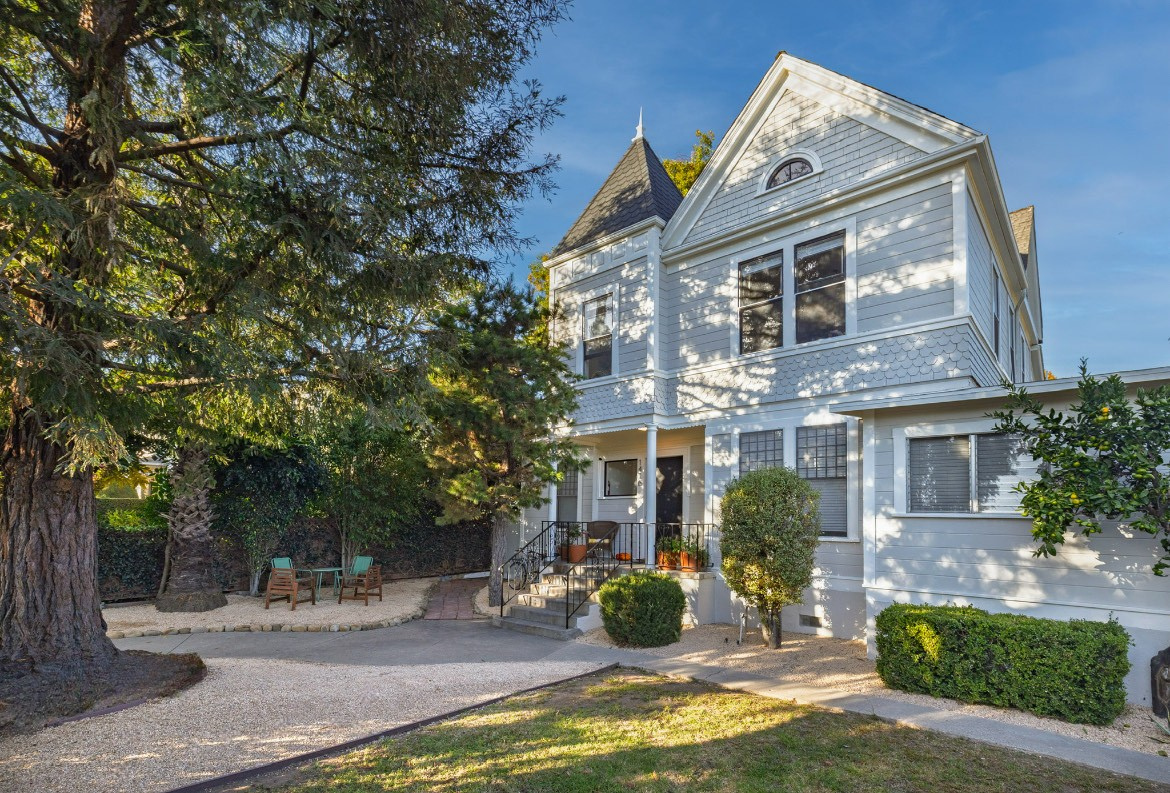 A gravel path leads to a building entrance with chairs, surrounded by trees and shrubs.