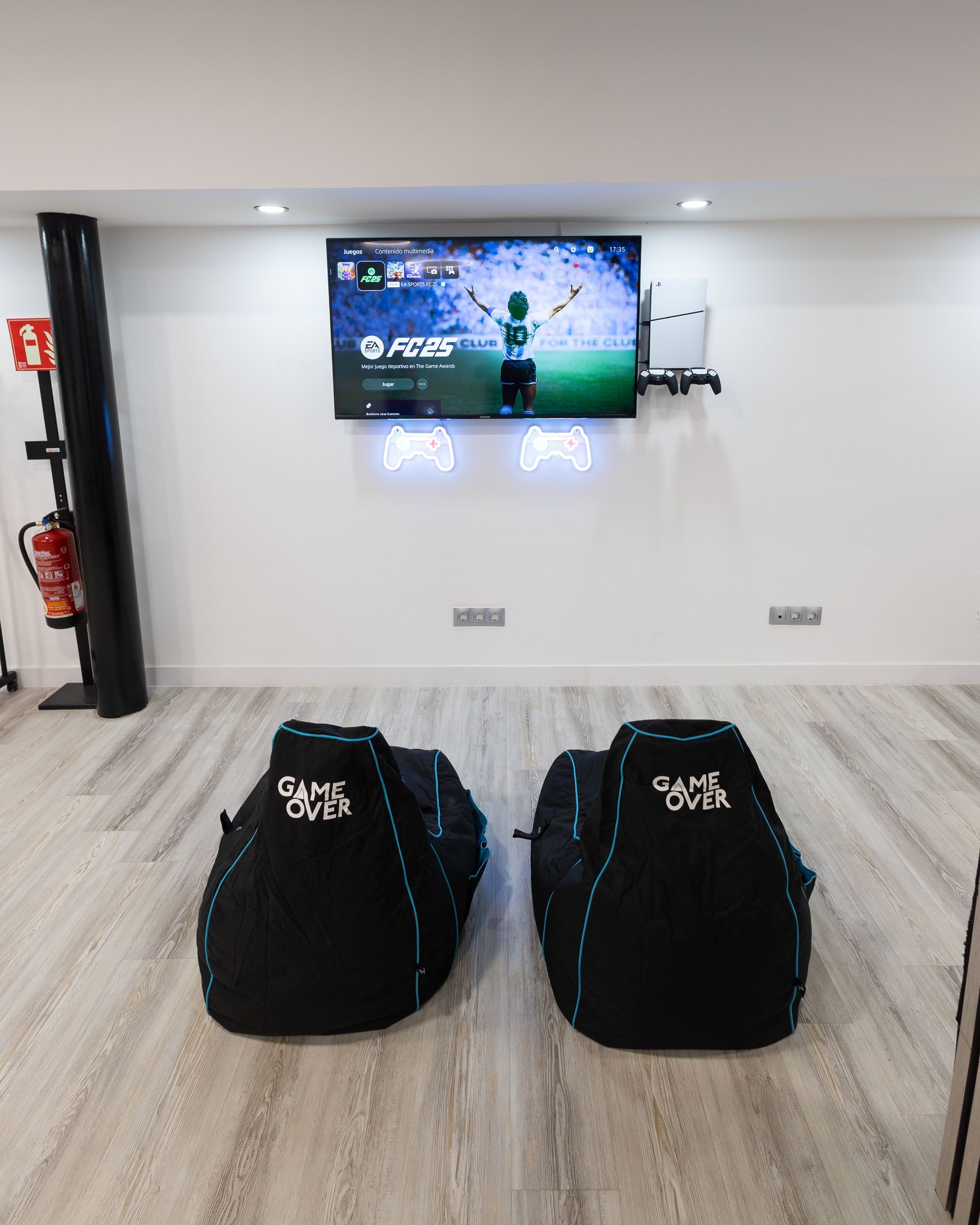 Dos bolsas de lona negras sobre un suelo alfombrado frente a un televisor montado en la pared en una habitación moderna.