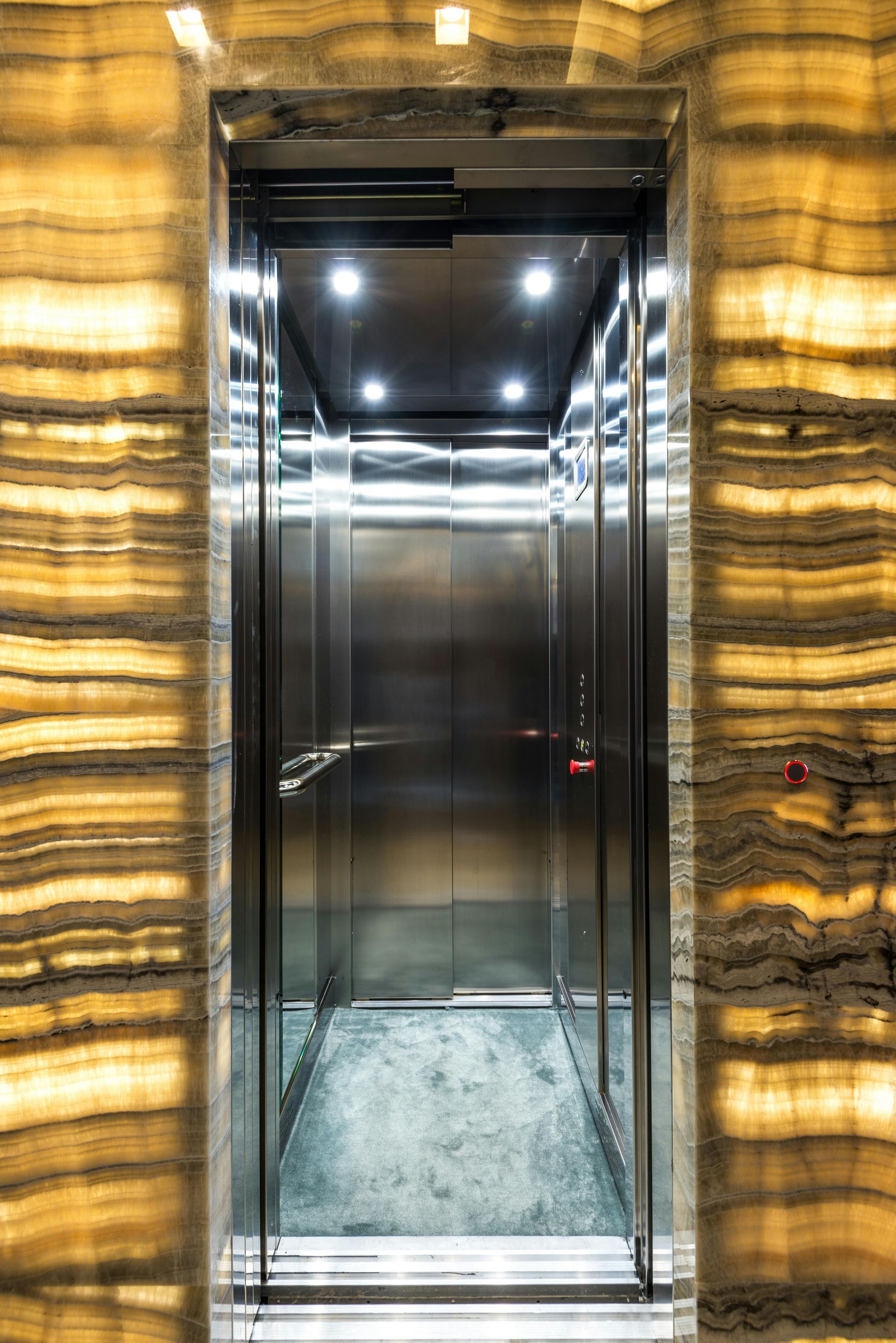 A stainless steel elevator with a marble wall behind it