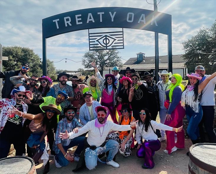 A group of people enjoying party bus services are posing for a picture in front of a sign that says treaty oak.