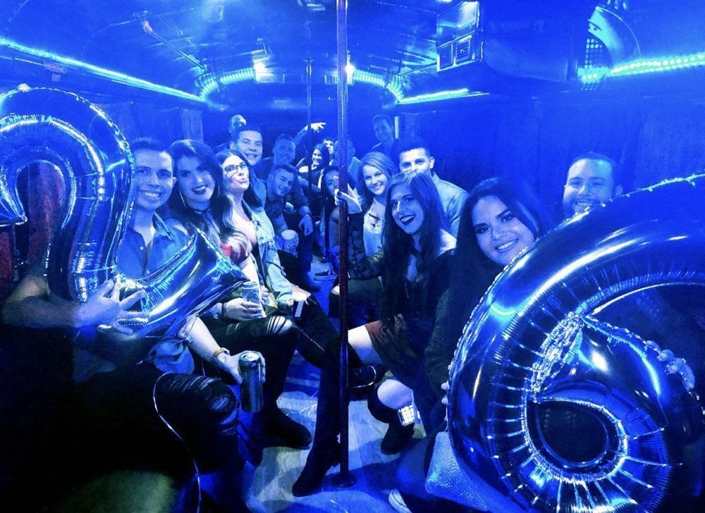 A group of people are sitting on a party bus holding balloons.