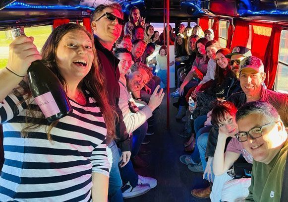 A group of people are sitting on a bus holding bottles of champagne.