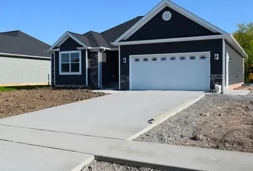 New concrete driveway leading to a modern dark grey home with a garage.