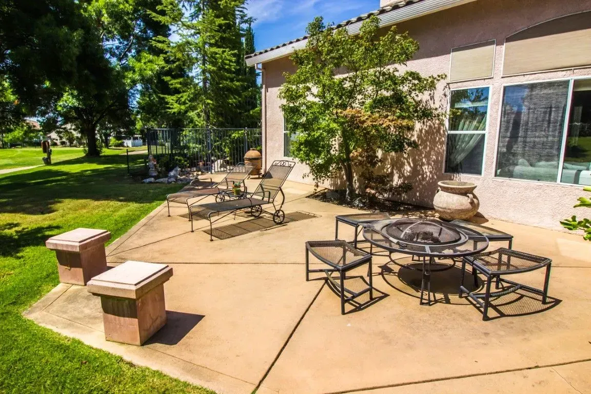 Spacious backyard concrete patio with outdoor furniture and landscaping.