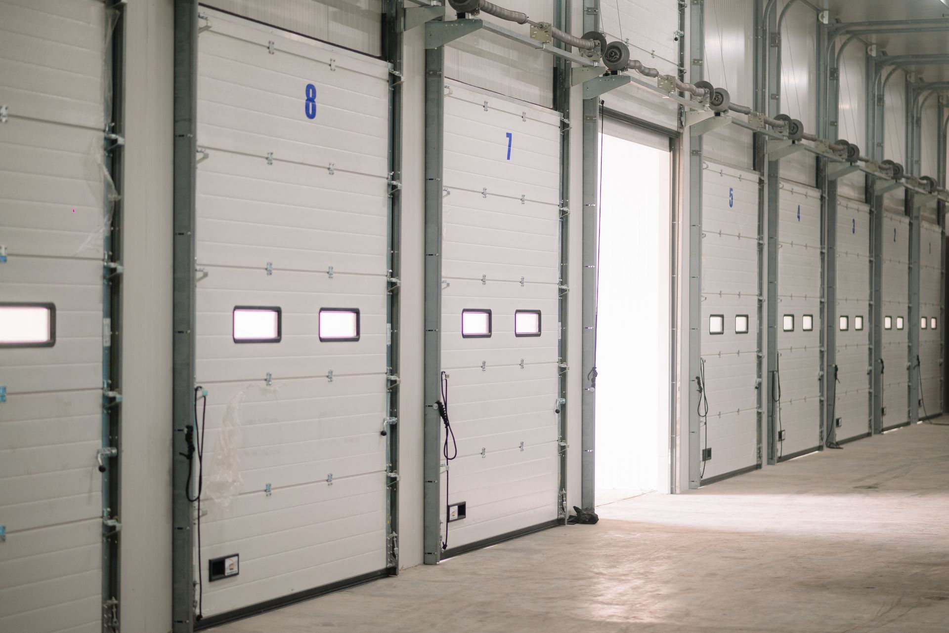 A modern warehouse loading bay with multiple numbered sectional overhead doors. A modern warehouse loading bay with multiple numbered sectional overhead doors.