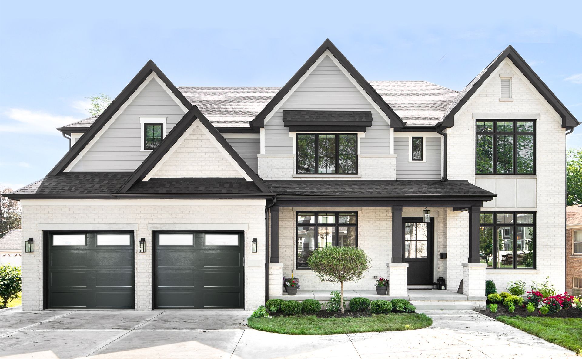 Modern two-story house with grey and white exterior. Black accents on windows, roof, and garage doors. Landscaping in front.