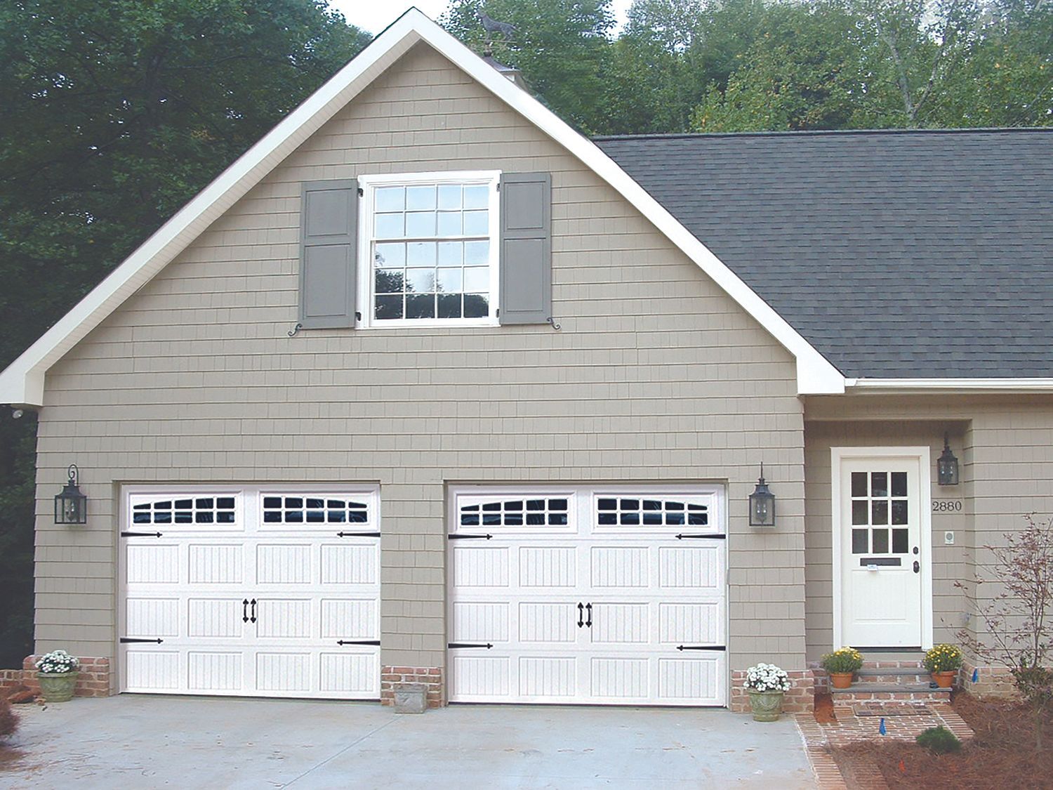 Tan house with two white garage doors, a white front door, and a window.