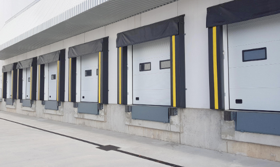 Exterior of a building with a glass garage door open to display white chairs and tables.