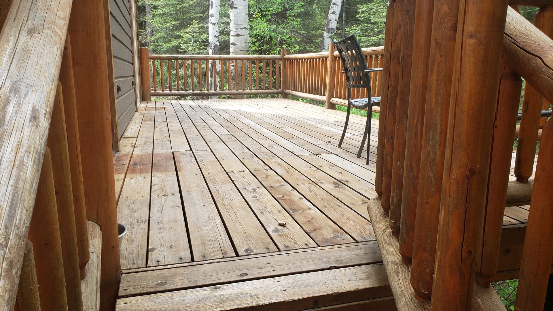 A wooden deck with a chair and stairs leading to it