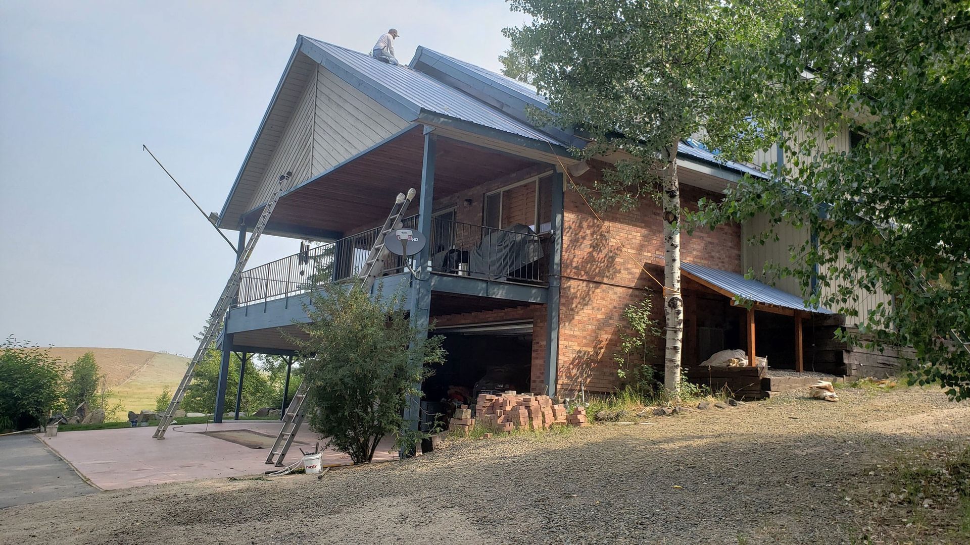 A large brick house with a blue roof is surrounded by trees.