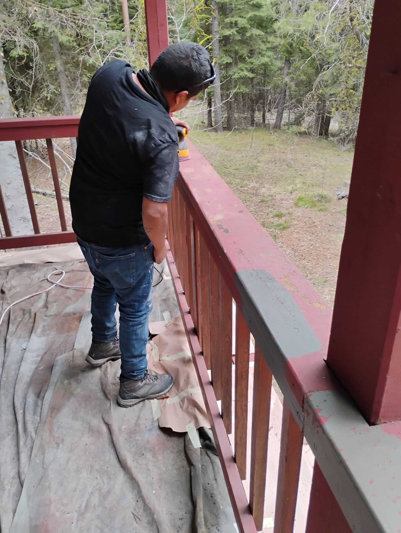 Person on a porch leaning over the railing, looking toward a wooded yard.